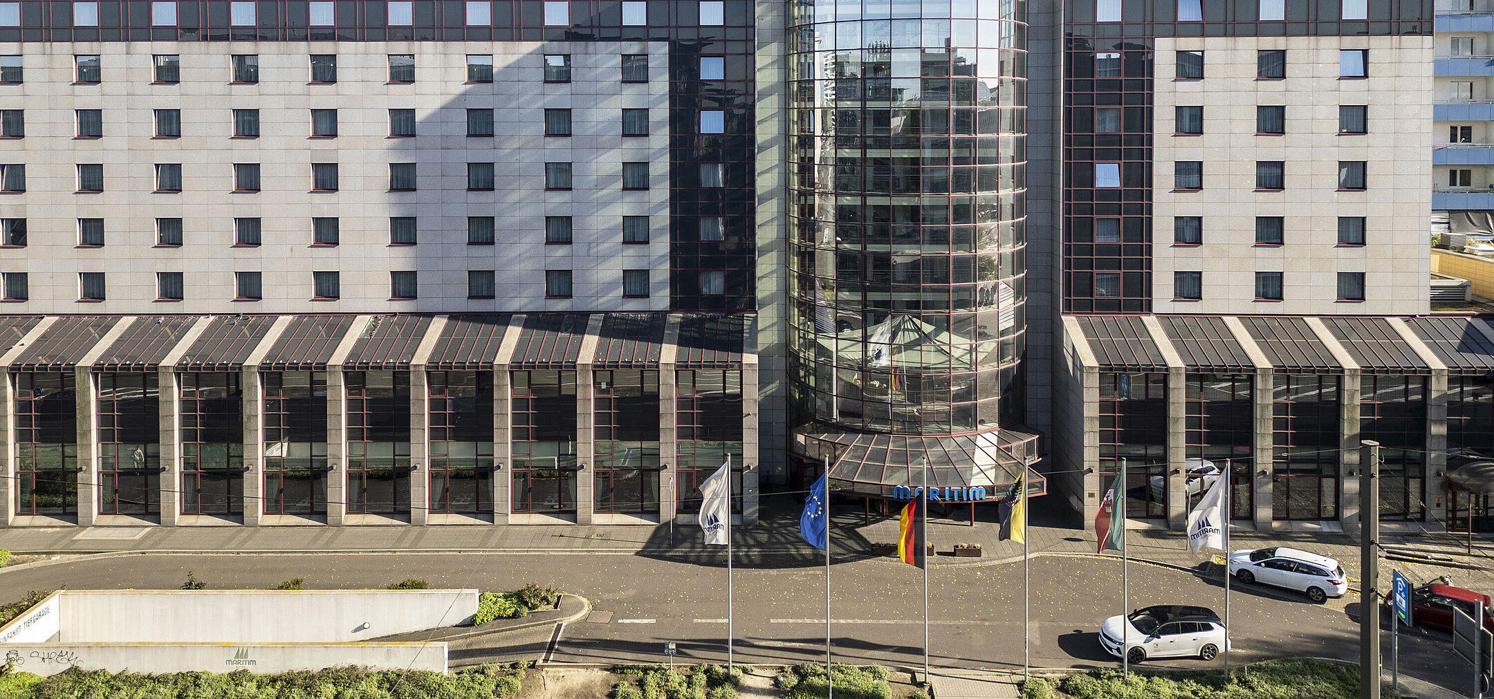 Front view of the Maritim Hotel with modern glass facade and flags at the entrance, showcasing its central and representative architecture.