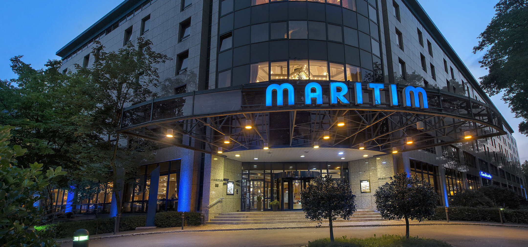 Exterior view of Maritim Hotel Bremen at dusk, illuminated logo and modern architecture.