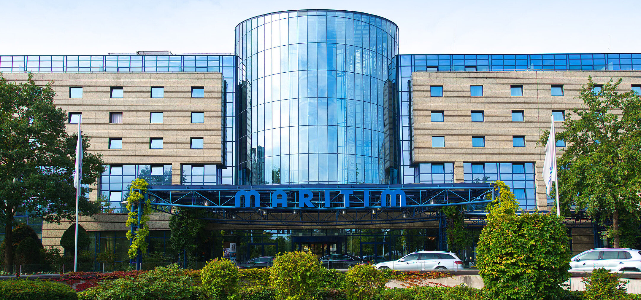 Exterior view of the Maritim Hotel Bonn with a modern glass facade and well-kept garden in the foreground.