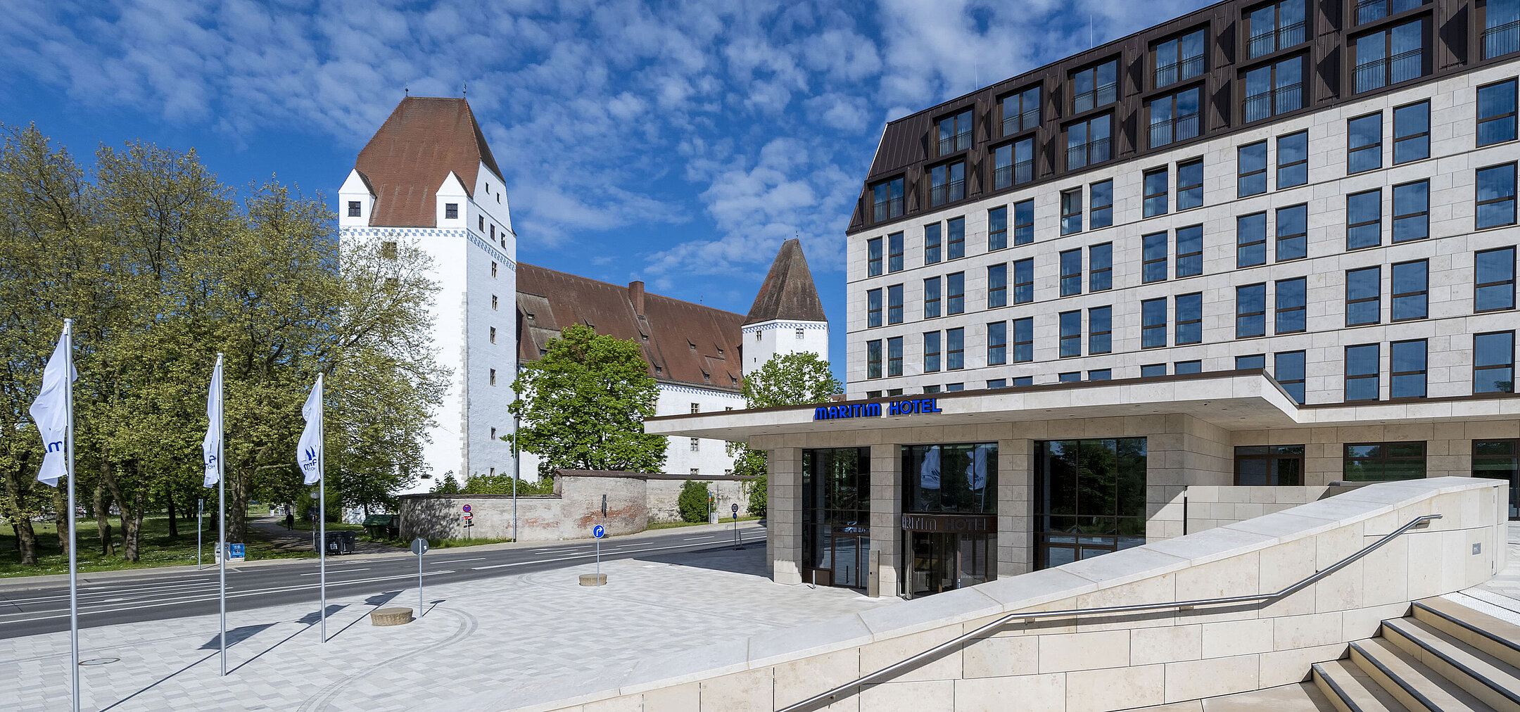 The modern Maritim Hotel Ingolstadt with the historic Neues Schloss in the background and a welcoming entrance.