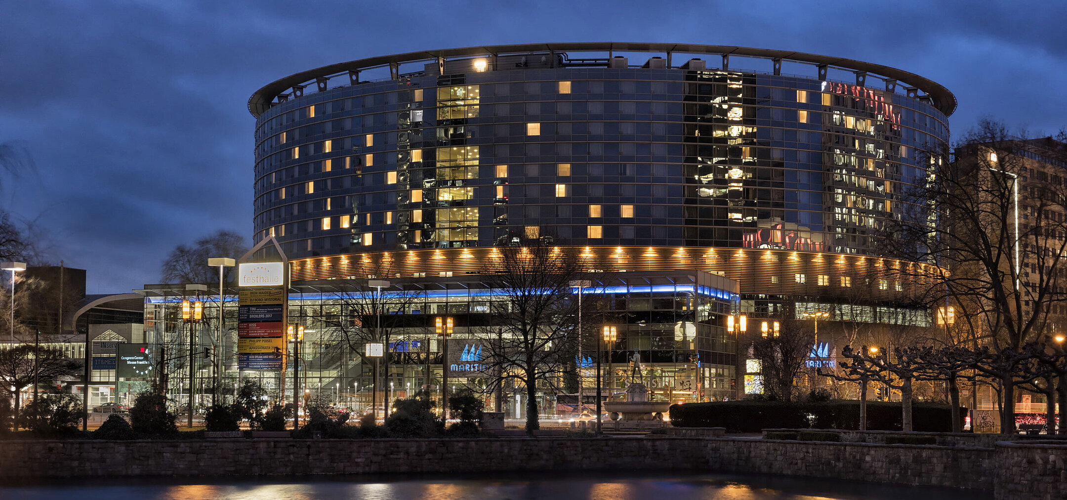 Maritim Hotel Frankfurt at night with illuminated glass facade and reflection in the calm pond.