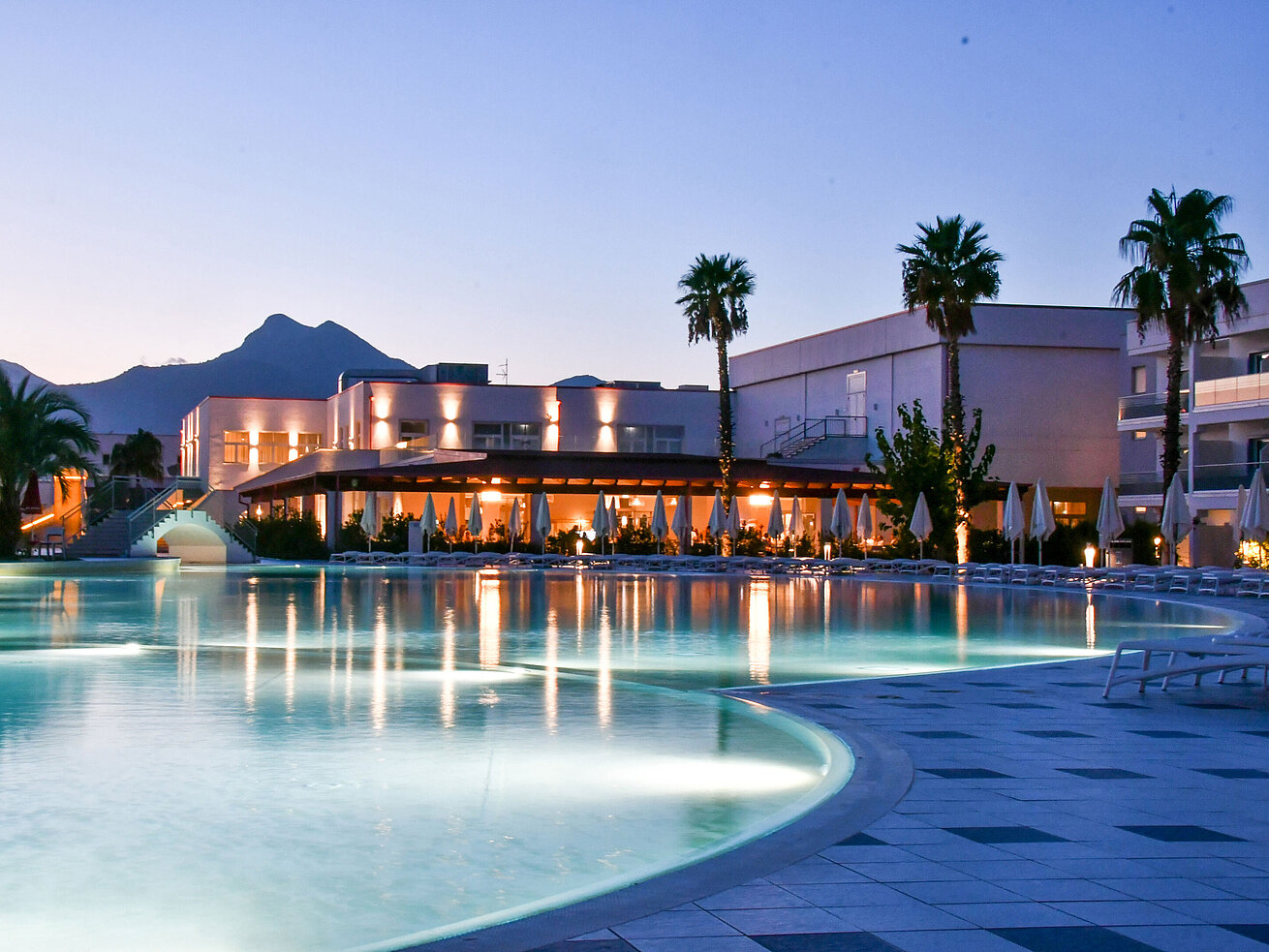 Evening lights at the pool of Maritim Resort Calabria with palm trees and mountain backdrop