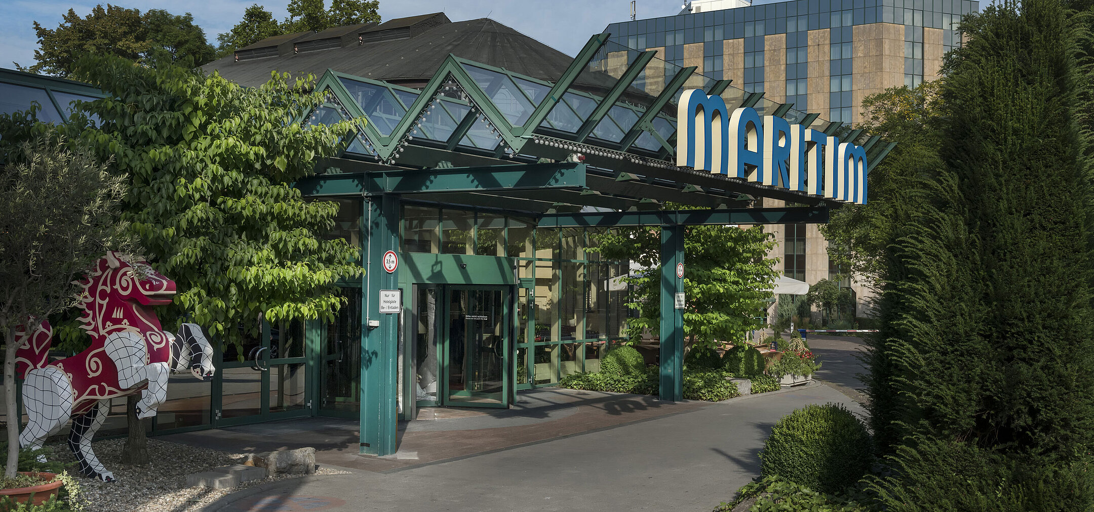 Main entrance of Maritim Hotel Stuttgart with glass roof, green facade and Maritim logo