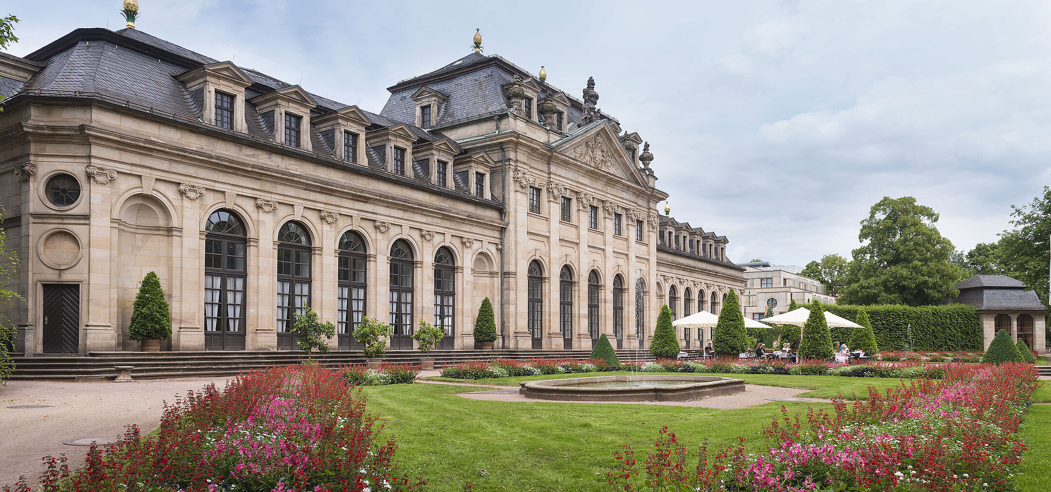 The historic Orangerie in Fulda with a baroque facade, staircase, and blooming garden in the foreground.